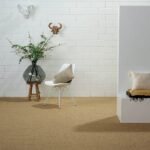 A modern room with white brick walls featuring a large tan sisal carpet, a white chair, and decorative plants.