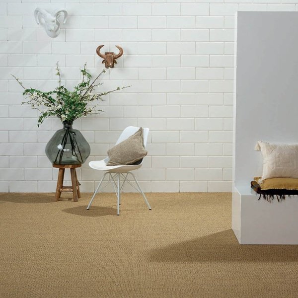 A modern room with white brick walls featuring a large tan sisal carpet, a white chair, and decorative plants.
