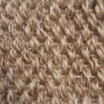 Close-up of a textured jute rug featuring a mix of warm tan and darker brown fibers.