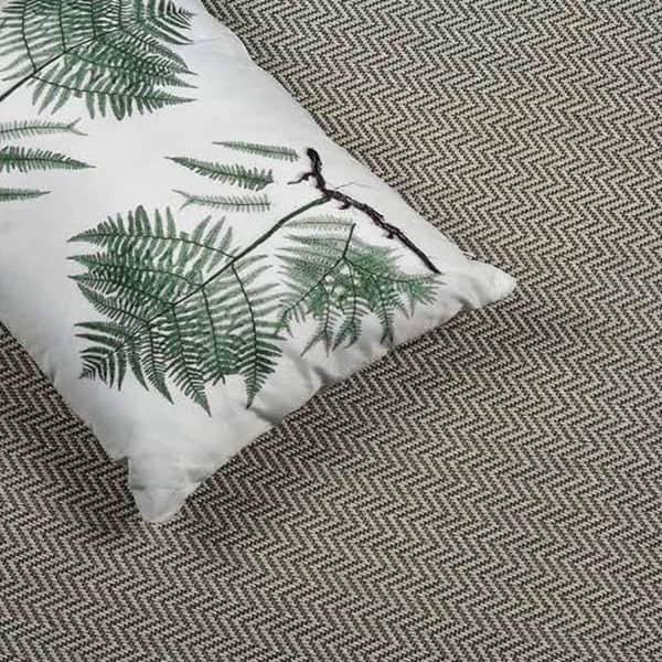 Fern-patterned cushion on a brown herringbone carpet.