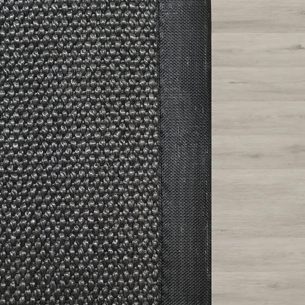 Top-down view of a dark grey textured rug with a black border on light wood flooring.