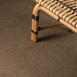 brown-textured-sisal-rug-featuring-the-leg-of-a-light-colored-rattan-chair.